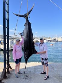 Two anglers proudly displaying a large Marlin at the marina after a successful fishing trip.