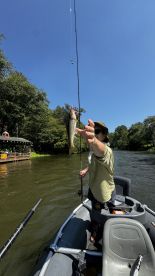 Angler reeling in a Largemouth Bass while fishing from a small boat on a sunny day.