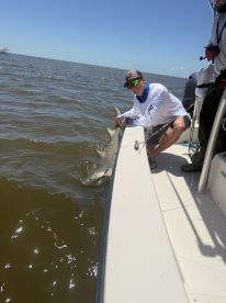 Angler actively reeling in a shark while fishing from a boat in a coastal waterway.