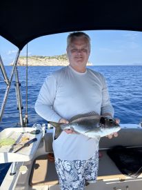 An angler proudly displaying a freshly caught fish while aboard a boat in a scenic coastal setting.