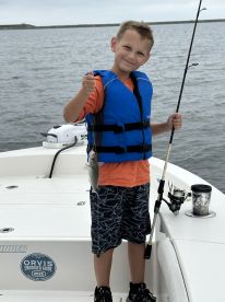 A young angler proudly displaying a small fish while fishing on a boat, wearing a life jacket, showcasing a fun day on the water.
