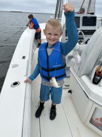 A young angler proudly displaying his catch while fishing from a boat, wearing a life jacket and enjoying a day on the water.