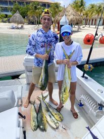 Two anglers proudly displaying their catch of Mahi Mahi on a fishing charter, with a tropical backdrop and clear waters.