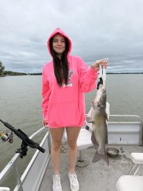 A young angler proudly displaying a large catfish while fishing on a calm lake, showcasing a relaxed day on the water.