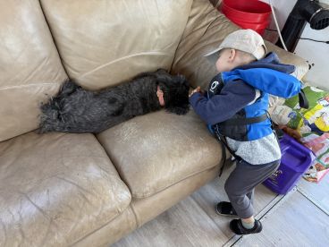 A young child in a life jacket interacts with a sleeping dog on a boat's couch, showcasing a cozy moment during a fishing trip.