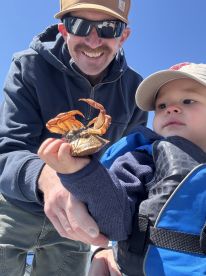 A young child and an adult proudly displaying a crab while enjoying a day on the water, showcasing a fun family fishing experience.