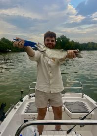 Angler proudly displaying a large fish while fishing from a small boat on a calm waterway.