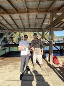 Two anglers posing with thumbs up at a dock, showcasing camaraderie after a fishing trip.