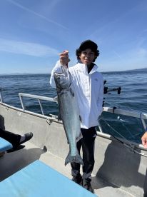 A young angler proudly displaying a large salmon while fishing on a boat in open waters.