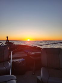 A serene sunset view from inside a fishing boat, showcasing the seating arrangement and tranquil waters.