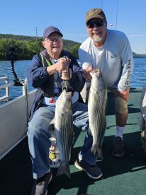 Two anglers proudly displaying their catch of striped bass while enjoying a sunny day on the water.