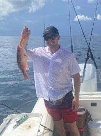 An angler proudly displaying a large Snapper while fishing on a sunny day in open waters.