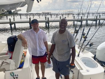 Two anglers enjoying their time on a fishing boat, showcasing the comfortable seating and fishing gear setup in a scenic waterfront environment.