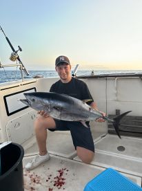 An angler proudly displaying a large Bluefin Tuna aboard a fishing boat during a sunset trip.