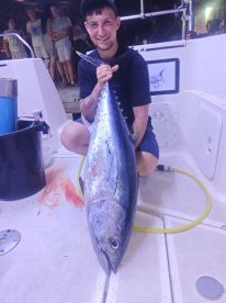 A proud angler displaying a large Bluefin Tuna aboard a fishing boat, with spectators in the background.