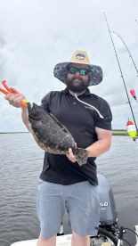 Angler proudly displaying a Flounder while fishing on a boat, showcasing a successful day on the water.