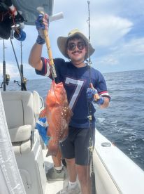 An angler proudly displaying a large Red Grouper while fishing on a boat in open waters.