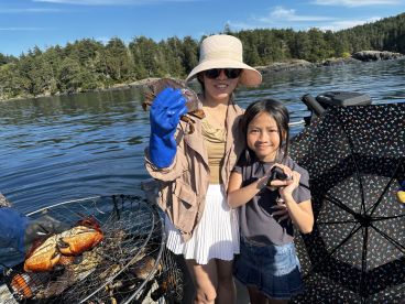 A mother and daughter proudly displaying their catch of crabs while enjoying a sunny day on the water, surrounded by a scenic coastal backdrop.