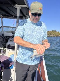 An angler on a boat carefully handling a freshly caught fish, showcasing the excitement of fishing in a scenic waterway.
