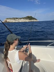 A woman fishing from a boat near a scenic island, showcasing a relaxed fishing environment with clear blue waters.