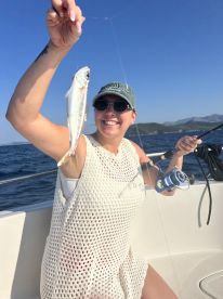 A smiling angler proudly displaying a freshly caught fish while fishing on a sunny day at sea.