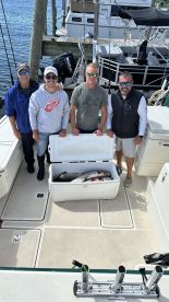 Group of anglers posing on a boat with a cooler containing freshly caught fish, showcasing a successful fishing trip.