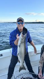 An angler proudly displaying a large Lake Trout while fishing on a boat, showcasing a beautiful day on the water.