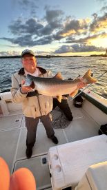 An angler proudly displaying a large trout on a fishing boat during a sunset outing.