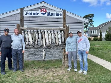 Group of anglers proudly posing in front of a catch board displaying multiple salmon after a successful fishing trip at Pointe Marine.