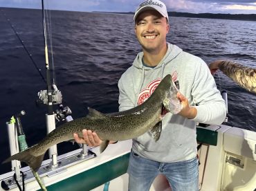 Angler proudly displaying a large Speckled Trout while fishing on a boat, showcasing a successful day on the water.