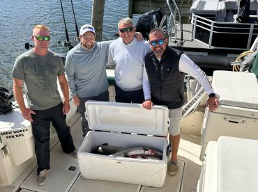 Four anglers posing on a boat with a cooler containing freshly caught fish, showcasing a successful fishing trip.