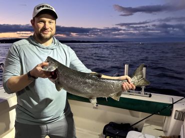 Angler proudly displaying a large Trout while fishing at sunset on a boat.