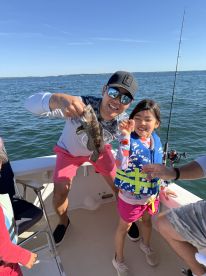 A proud father and daughter duo showcasing their catch, a Black Sea Bass, while enjoying a sunny day on the water.