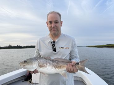 An angler proudly displaying a large Redfish while fishing in a serene coastal environment.