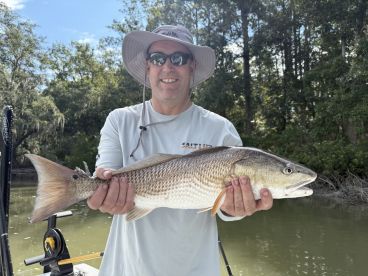 An angler proudly displaying a large Redfish while fishing in a scenic river environment.