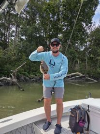 Angler proudly displaying a Flounder while fishing from a boat in a scenic coastal environment.