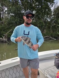 Angler proudly displaying a Black Drum caught while fishing in a scenic river environment.