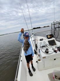 A young angler proudly displaying a striped bass while fishing from a boat in a calm waterway.