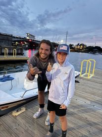 Two young anglers posing together at the dock during twilight, with a small boat in the background.