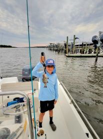 A young angler proudly displaying a caught fish while aboard a boat in a calm waterway, showcasing a fun fishing experience.