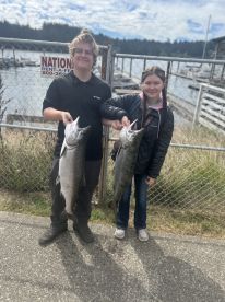 Two young anglers proudly displaying their catch of Salmon at the dock, showcasing a successful fishing trip.