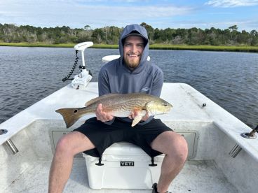 Angler displaying a Redfish while seated on a boat in a scenic coastal environment.