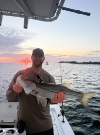 Angler proudly displaying a large Snook against a stunning sunset backdrop while fishing from a boat.