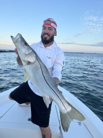 Angler proudly displaying a large Snook while on a fishing boat, showcasing a successful catch during a coastal fishing trip.
