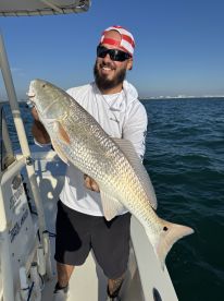 Angler proudly displaying a large Redfish while on a boat, showcasing a successful fishing trip in clear waters.