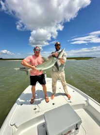 Two anglers proudly displaying a large shark on a boat during a fishing trip in a coastal waterway.