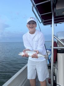 Young angler proudly holding a Speckled Trout while fishing from a boat, showcasing a successful catch during a coastal fishing trip.