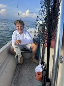 A young angler smiles while holding a caught fish aboard a small boat, enjoying a day of fishing in calm waters.