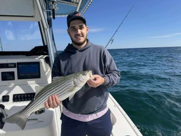 Angler holding a striped bass aboard a fishing boat, showcasing a successful catch during a day on the water.