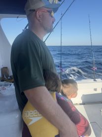A father and two children enjoying a fishing trip on a boat, with the ocean in the background and fishing rods visible.